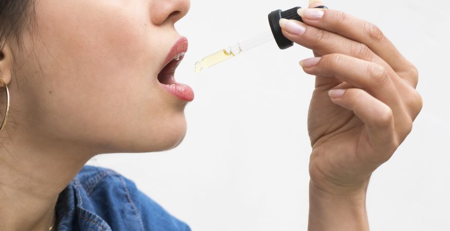 woman-holding-glass-pipette-dropping-bud-and-tender-cbd-oil-into-mouth