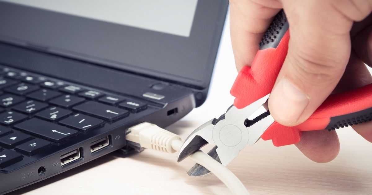 Red cable cutters cutting a laptop ethernet cable. 