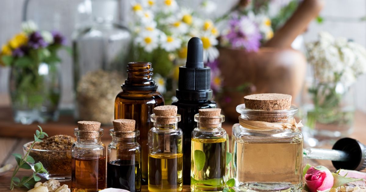 variety of essential oils and herbs on a table with flowers in the background
