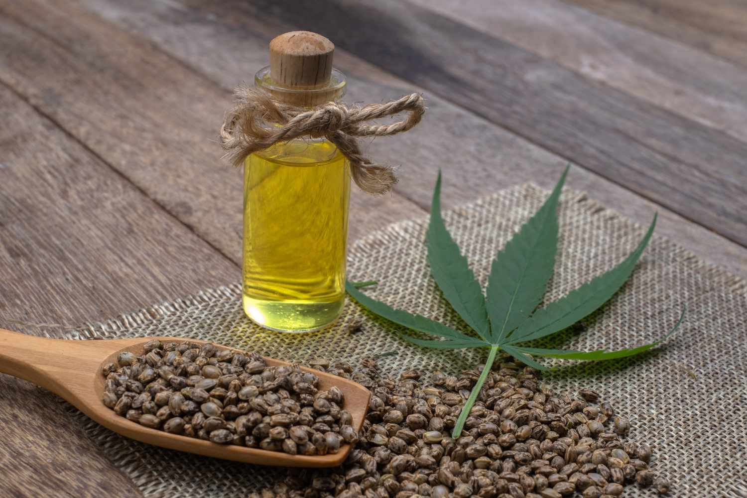 hemp-oil-in-a-glass-bottle-tied-with-a-bow-hemp-seeds-in-a-wooden-spoon-on-the-table--the-concept-of-bringing-hemp-oil-extracted-as-a-medicine-by-natural-methods--doctors-and-marijuana--1213507155-f7c56b525a214135ad694821317ad106.jpg