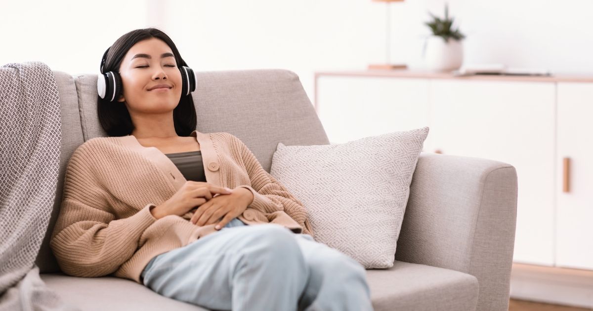 Woman listening to music through headphones while sitting on a beige sofa.