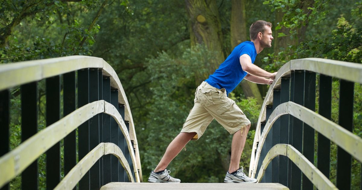 man in blue thirt stretching on a wooden bridge