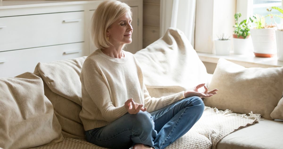A woman sitting on a beige sofa meditating. 