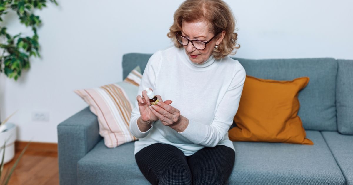 woman sat on a blue couch reading the label of her cbd bottle