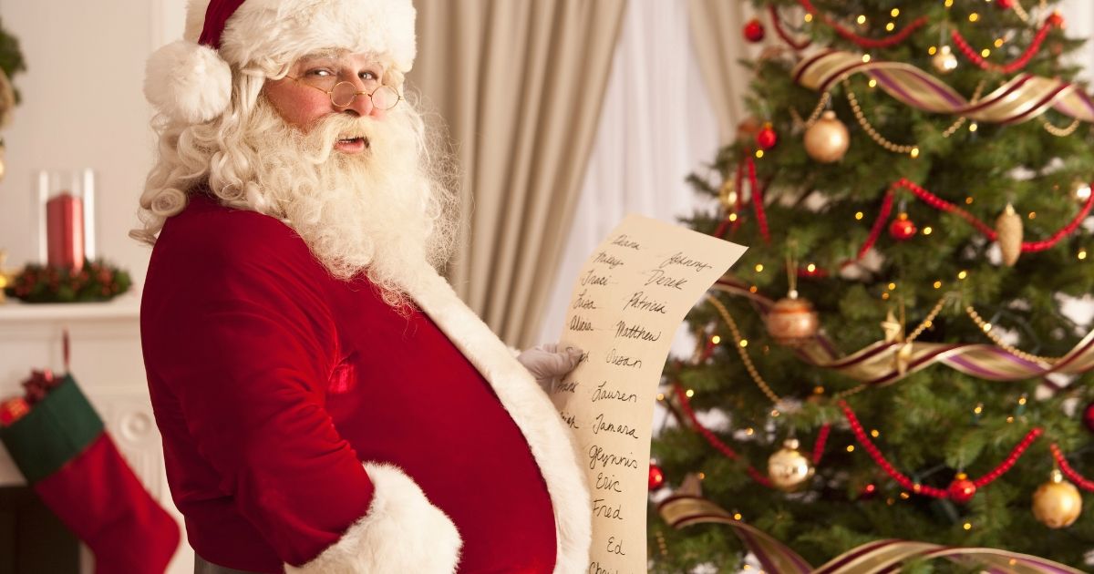 santa checking his list in front of a christmas tree