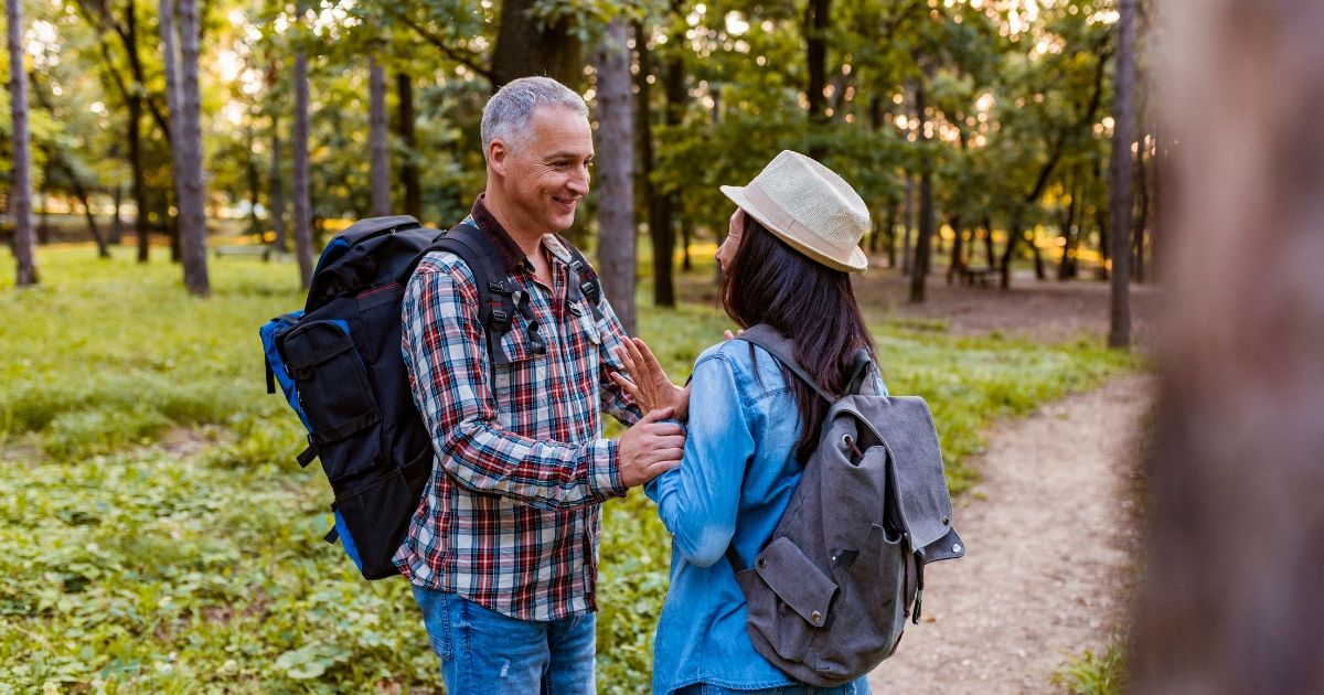 A man and a woman outside in the woods. They are both wearing backpacks. 
