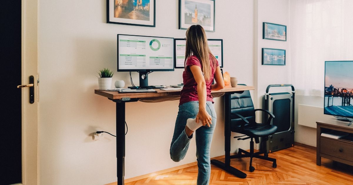 woman in home office standing at desk and stretching