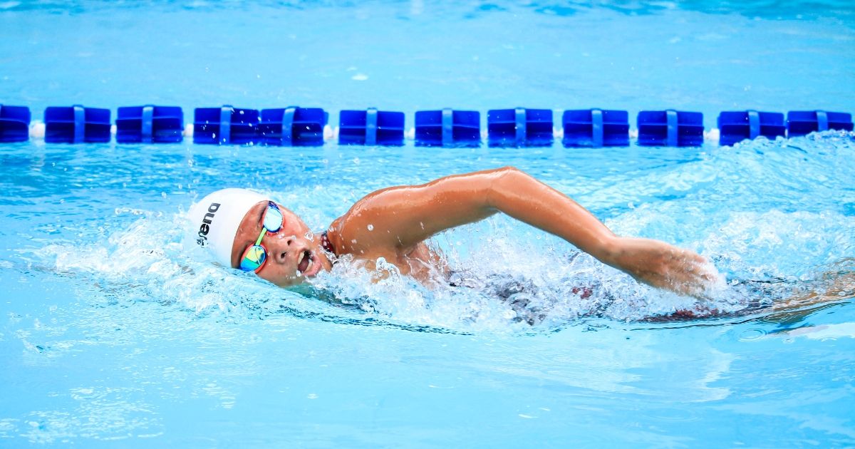 a person swimming in a swimming pool. They are wearing a white swimming cap and goggles. 