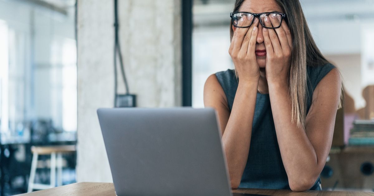 woman looking tired and rubbing her eyes in front of her laptop